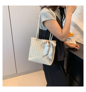 Detail of beige straw tote bag with V-weave pattern and decorative heart-printed silk scarf