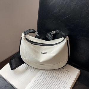 White crescent shoulder bag with black strap on a book, minimalist commuter fashion