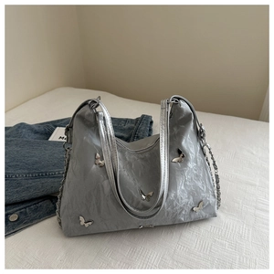 Zilveren geplooide shopper met vlinderbedels en kettingriemen op denim achtergrond