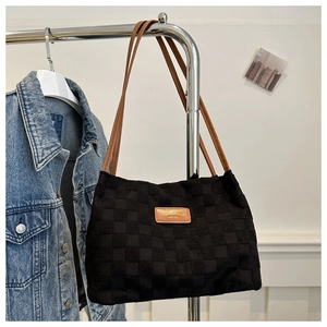 Detail of black woven tote bag with brown leather straps and branded metal tag
