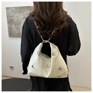 Detail of cream eel-textured tote bag featuring metallic butterfly charms and shoulder strap