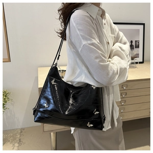 Detail of black glossy PU leather hobo bag with silver butterfly charms on model
