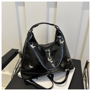Close-up of black glossy patent leather tote bag with silver butterfly metal charms