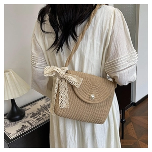Detail of straw woven crossbody bag featuring lace bow and pearl button closure