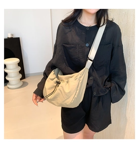 Side view of a beige drawstring crossbody dumpling bag on a model for urban casual style