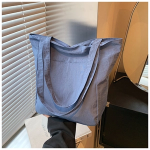 Detail of blue oversized nylon tote bag with side pocket on a desk setup