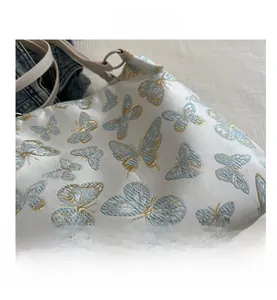 Detailed view of exquisite blue and gold butterfly embroidery on white shoulder bag