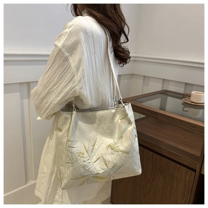 Macro detail of high-quality embroidery featuring birds and leaves on a cream tote bag