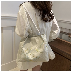 Detail of floral bird embroidery on beige fabric tote bag with slim white shoulder strap