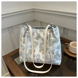 Detailed embroidery of gold and blue butterflies on a light blue satin tote bag surface