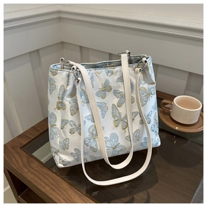Detail of blue jacquard tote bag with golden butterfly embroidery and leather straps