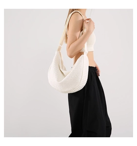 Side view of white pleated crescent bag showing textured fabric and wide strap on model