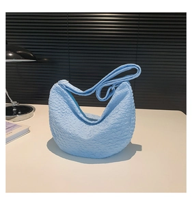 Detail of light blue crescent bag with pleated fabric texture and minimalist strap