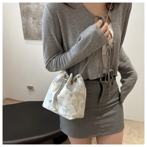Detail of white bucket bag with blue butterfly prints and elegant pearl chain strap