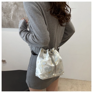 Detail of white bucket bag featuring blue butterfly embroidery and pearl tassels