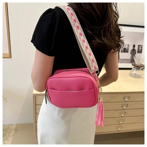 Detail of pink crossbody bag with litchi grain texture and woven strap shown on model
