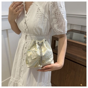 Detail of off-white drawstring bucket bag with golden leaf embroidery and pearl accents