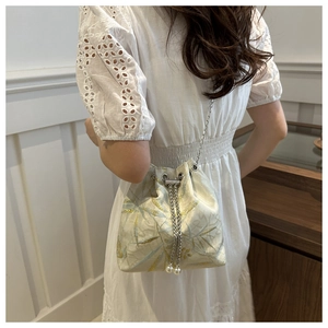 Detail of blue and gold bamboo jacquard bucket bag with pearl drawstring and silver chain