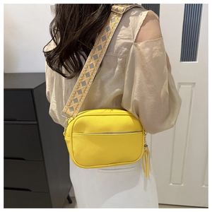 Detail of yellow lychee leather camera bag with wide geometric jacquard strap and tassel