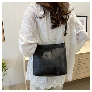 Detail of black patchwork leather shoulder bag with gold buckle on a model in white blouse