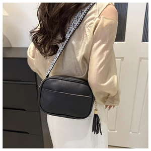 Detail view of black pebble leather crossbody bag with geometric woven strap and long tassel