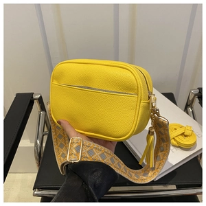 Detail of yellow lychee texture crossbody bag with geometric woven strap and tassel