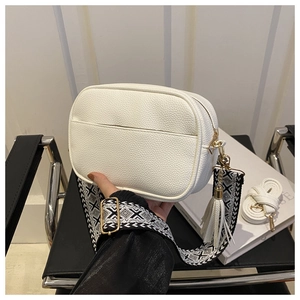 Detail of white lychee leather handbag featuring decorative jacquard strap and tassel