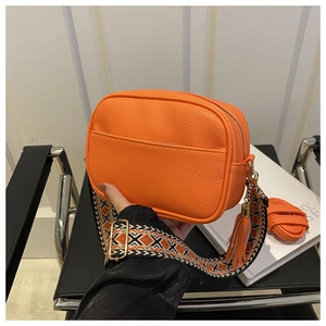 Detail of orange pebble leather crossbody bag with ethnic style wide woven strap and tassel