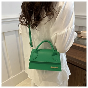 Detail of green crossbody bag featuring golden letter logo and adjustable shoulder strap