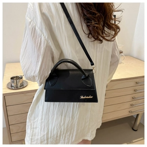 Detailed view of a black leather crossbody bag with gold logo on a white pleated dress
