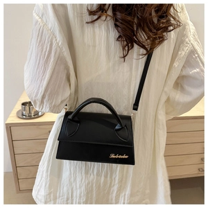 Detail of minimalist black crossbody bag with gold logo on a white shirt background