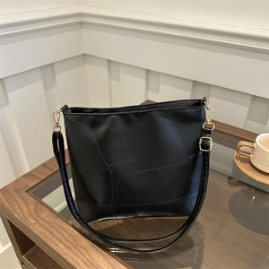 Black soft PU leather patchwork tote bag with gold hardware on a wooden table