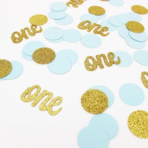 Gros plan de lettres 'one' pailletées dorées et confettis bleus pour premier anniversaire
