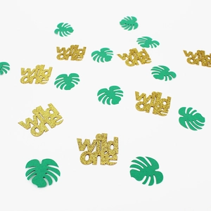 Close-up of Wild One glitter gold lettering and green monstera leaf party confetti