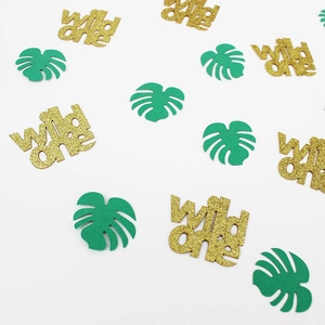 Macro detail of gold glitter wild one letters and green monstera leaf party confetti