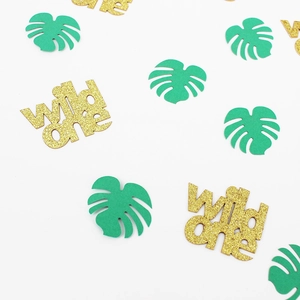 Close-up of golden glitter wild one confetti and green tropical palm leaves for party decor