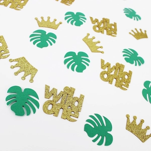 Detail of wild one confetti with glitter gold crowns and green tropical leaves