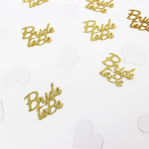 Close-up of gold glitter Bride to Be confetti and white heart paper decorations for bridal showers
