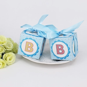 Light blue baby shower gift box with letter B and blue ribbon on white ceramic tray