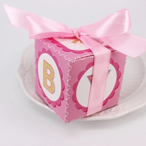Pink cubic baby gift box with satin ribbon bow and colorful polka dots on white plate