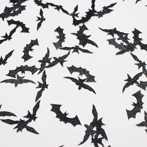 Glittery black bat confetti for Halloween party decor scattered on white background