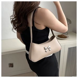 Detalle de bolso baguette beige con lazo metálico plateado llevado como bolso de hombro