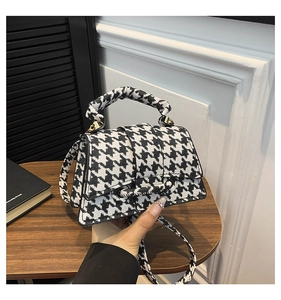 Close-up of small black and white houndstooth flap bag with chunky top handle and strap