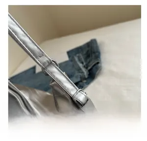 Detail of adjustable buckle and bow charm on silver metallic finish shoulder bag