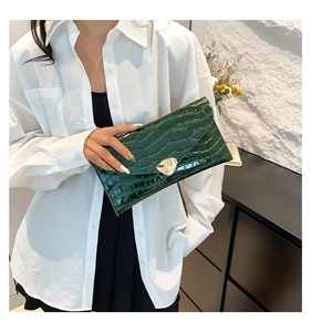 Gros plan sur la pochette enveloppe en cuir vert foncé à motif crocodile et fermoir