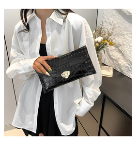 Détail d'une pochette enveloppe noire à motif crocodile avec boucle en métal doré chic