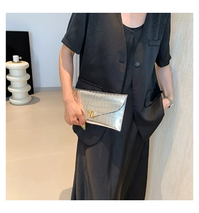 Détail d'une pochette enveloppe argentée à motif crocodile et boucle dorée ondulée