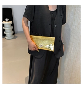 Gros plan d'une pochette dorée à texture crocodile avec fermoir en forme de feuille