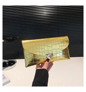 Détail d'une pochette dorée à motif crocodile avec une boucle en métal en forme de cœur