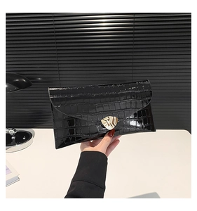 Détail d'une pochette enveloppe noire à motif crocodile avec un fermoir doré en feuille